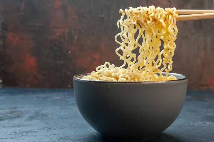 Bowl of instant noodles being lifted with chopsticks, representing unhealthy human things and fast food habits.
