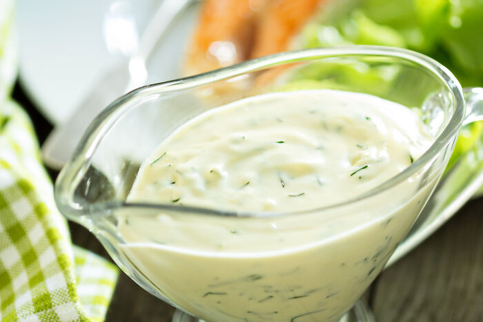 Glass bowl of creamy dressing with herbs, highlighting an example of unhealthy human things in food choices.