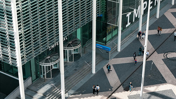 Aerial view of people walking outside a modern building with large pillars and the word Imperial on the facade. Aerial view of people walking outside a modern building with large pillars and the word Imperial on the facade.