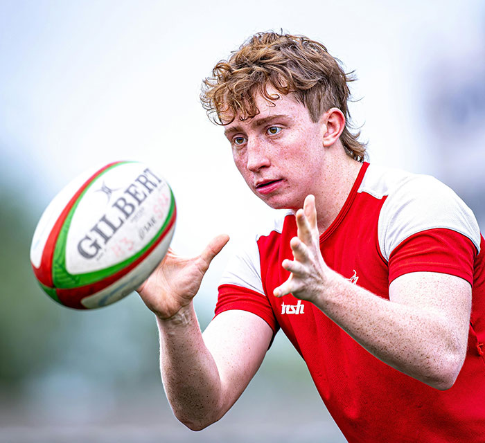 Teenage boy focused on catching a rugby ball wearing a red and white sports shirt outdoors. Teenage boy focused on catching a rugby ball wearing a red and white sports shirt outdoors.