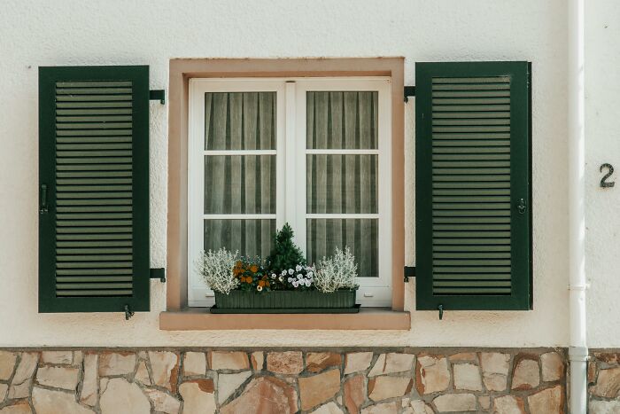 Window of elderly parents’ home with green shutters and flower box, symbolizing care and family support requests.