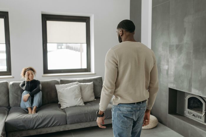 Husband refusing to help check on elderly parents’ home while wife sits on couch looking concerned.