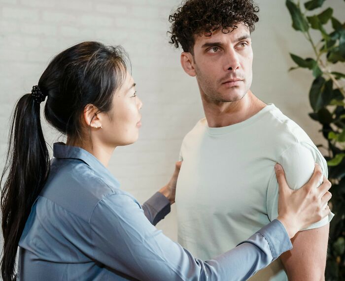 Wife asking husband to help check on elderly parents’ home while he refuses and looks frustrated indoors.