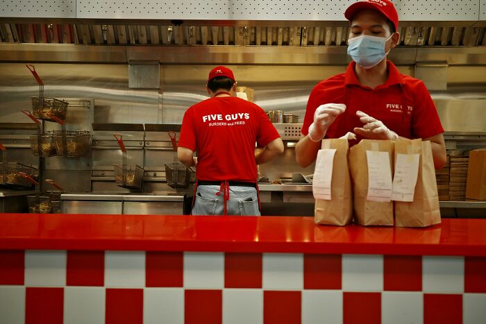 Two Five Guys employees preparing orders behind the counter revealing industry secrets inside fast food kitchens.