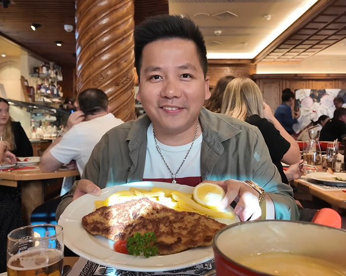 Vlogger smiling while holding a plate of food at a restaurant unaware he is sitting next to an A-list star nearby. Vlogger smiling while holding a plate of food at a restaurant unaware he is sitting next to an A-list star nearby.