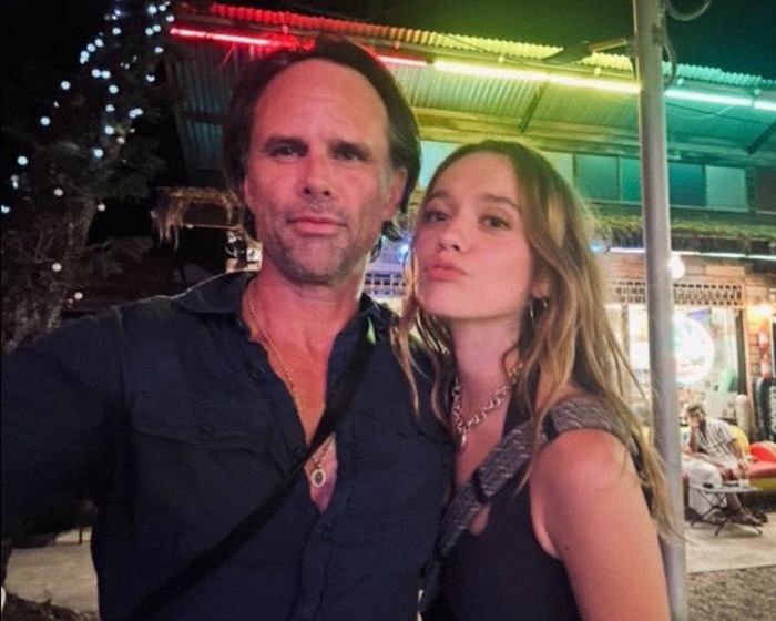 Walton Goggins and Aimee Lou Wood posing together outdoors at night with lights and a building in the background Walton Goggins and Aimee Lou Wood posing together outdoors at night with lights and a building in the background