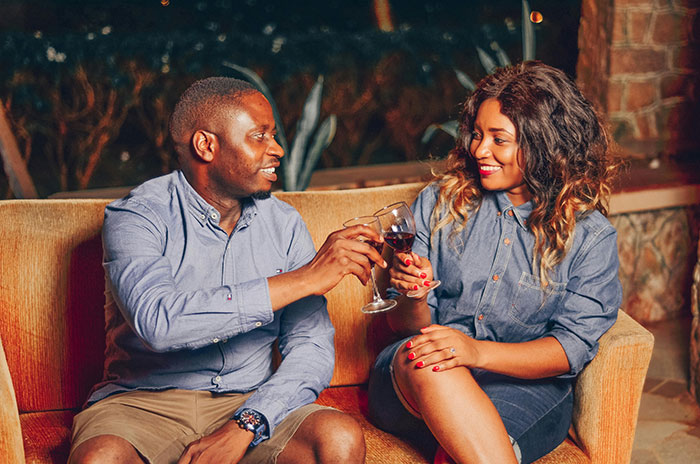 Couple toasting with wine glasses, smiling and enjoying a relaxed evening on a cozy sofa indoors.