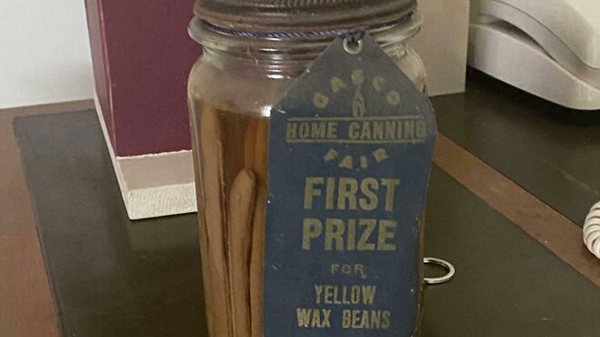 Glass jar with a vintage first prize tag for yellow wax beans found among bizarre things in an old house setting.