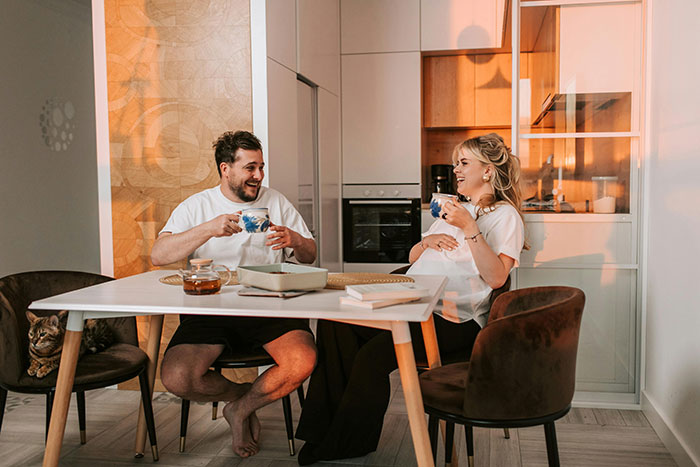 Man and wife laughing and drinking tea at a modern kitchen table, capturing a light moment in their relationship. Man and wife laughing and drinking tea at a modern kitchen table, capturing a light moment in their relationship.