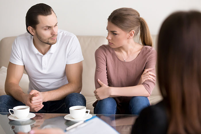 Man and wife sitting on couch looking upset during a tense conversation with a third woman present. Man and wife sitting on couch looking upset during a tense conversation with a third woman present.