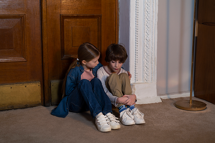 Two young siblings sitting on a floor inside an empty house, appearing sad and comforted by each other. Two young siblings sitting on a floor inside an empty house, appearing sad and comforted by each other.