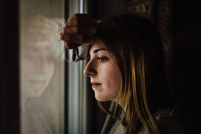 Young woman looks thoughtfully out a window, reflecting on her fiancé’s mom wedding dress and family dynamics. Young woman looks thoughtfully out a window, reflecting on her fiancé’s mom wedding dress and family dynamics.