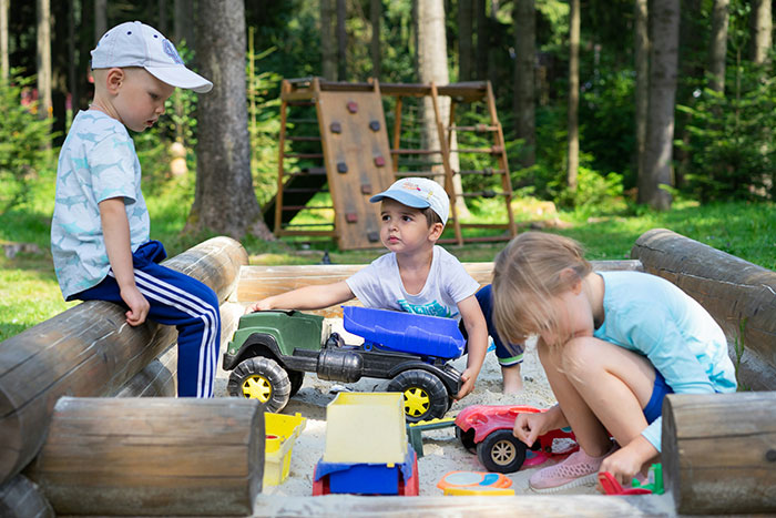 Three kids playing with toy cars in a sandbox outdoors, illustrating family drama and babysitting issues. Three kids playing with toy cars in a sandbox outdoors, illustrating family drama and babysitting issues.