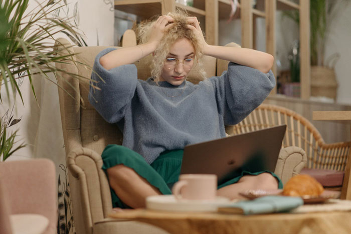 Young woman looking stressed during an interview task on laptop, realizing she got tricked while working from home.