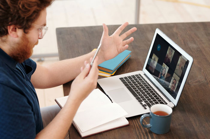 Man reacting shocked during a live interview task on laptop video call with open notebook and coffee mug nearby.