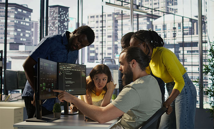 A diverse group of employees gathered around a computer screen discussing deployment rules and company policy changes. A diverse group of employees gathered around a computer screen discussing deployment rules and company policy changes.