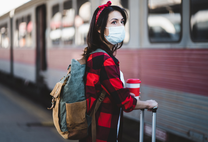 Woman wearing a face mask and carrying luggage at train station, representing best countries to live in 2025. Woman wearing a face mask and carrying luggage at train station, representing best countries to live in 2025.