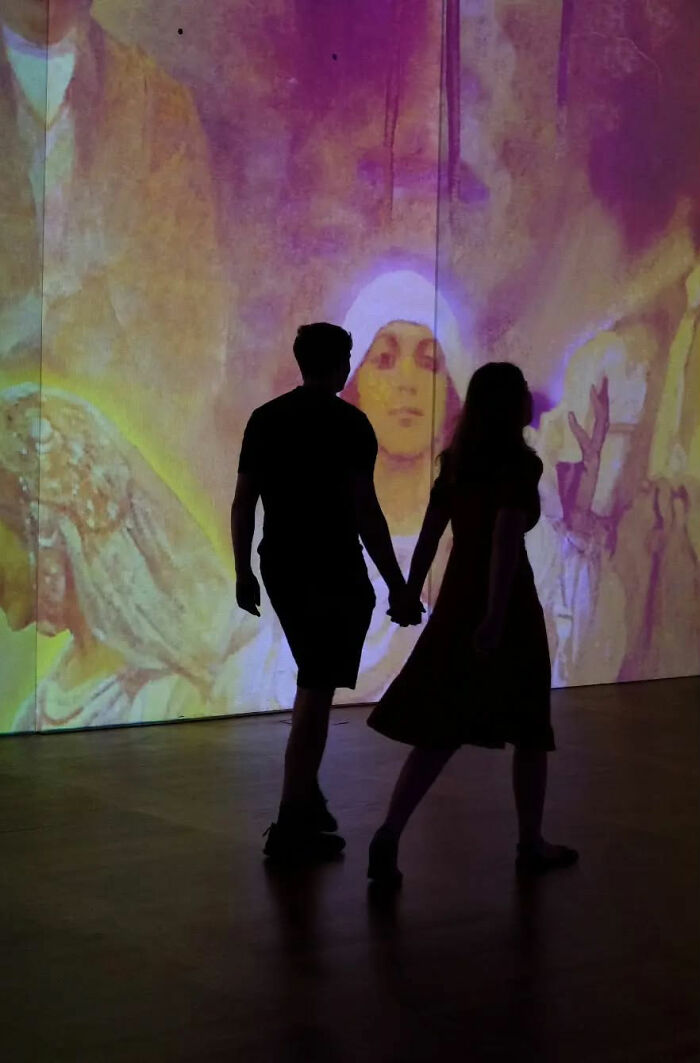 Silhouettes of a couple holding hands walking indoors with a colorful artistic projection in the background street shots.