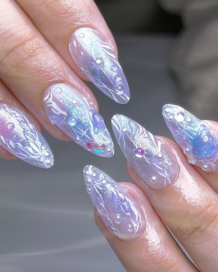 Shimmering 2025 summer nails with intricate pearl and glitter designs on long almond-shaped nails.