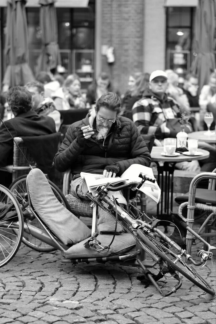 Man smoking and reading newspaper by recumbent bicycle at a café, a beautiful street shot capturing everyday life moments.