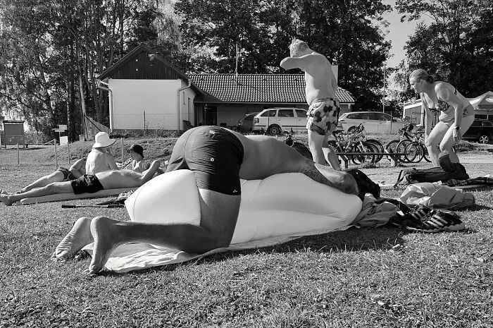 Black and white street shot capturing everyday life with people relaxing and interacting outdoors on a sunny day.