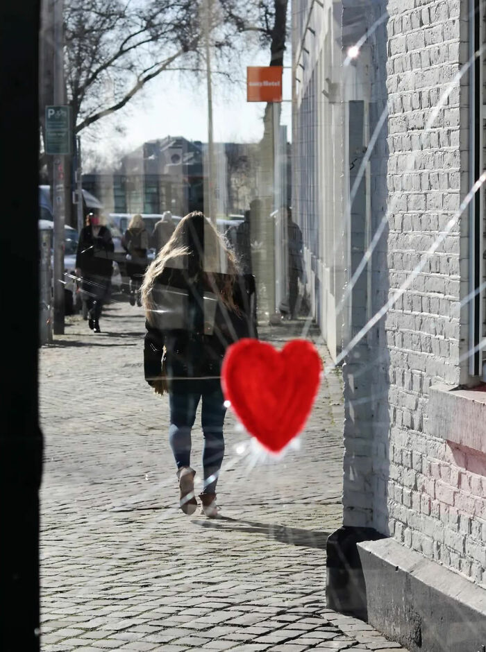 A street shot capturing a person walking on a cobblestone sidewalk with a red heart reflected on a glass window.
