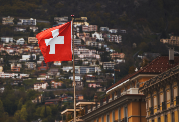 Swiss flag waving over a hillside town representing one of the best countries to live in 2025 with scenic views and urban living. Swiss flag waving over a hillside town representing one of the best countries to live in 2025 with scenic views and urban living.
