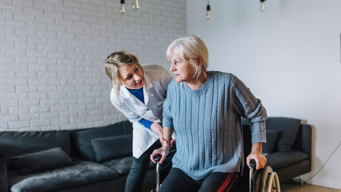 A healthcare professional assisting an elderly woman using a walker in a cozy living room setting.