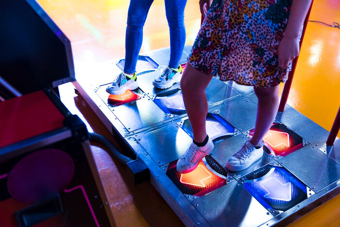 Two people playing a dance arcade game with illuminated arrow pads, highlighting a good trend slowly disappeared in gaming.