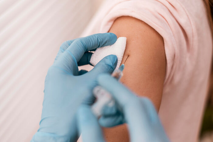 Close-up of a healthcare worker wearing gloves giving a vaccine injection to a person's upper arm.