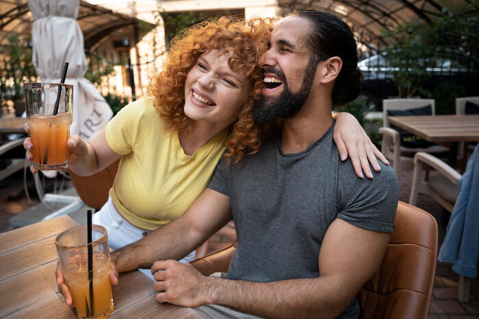 A couple enjoying drinks and laughing together on a casual date at an outdoor bar setting.