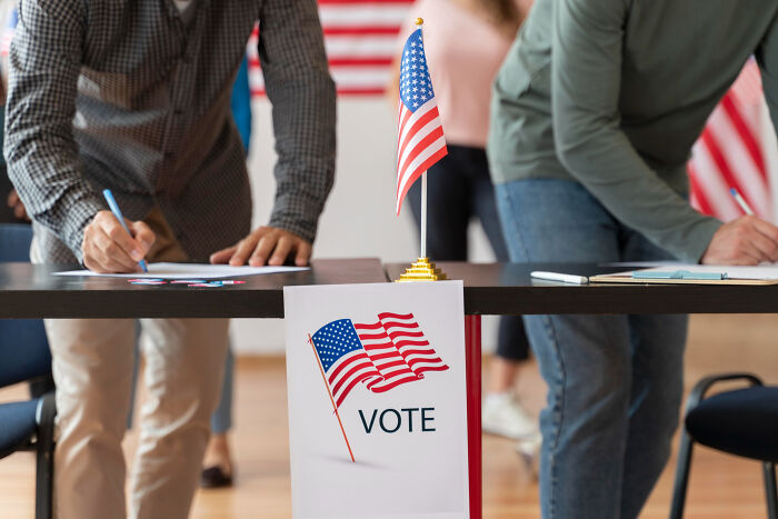 People casting ballots at a voting station with American flags, showing a good trend slowly disappeared in participation.