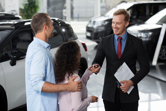 Car salesman handing car keys to a couple, illustrating professions people think attract the most awful people.