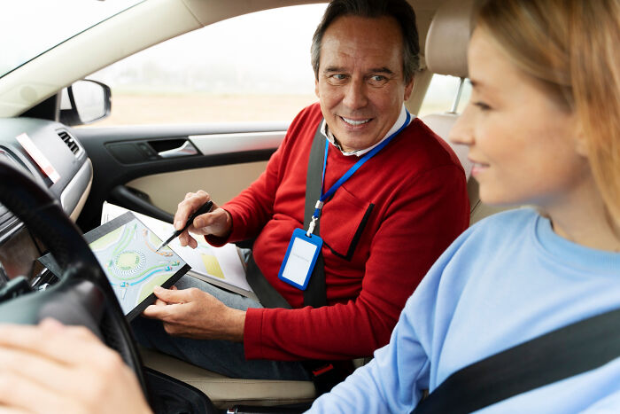 Driving instructor explaining road map to young woman in car, illustrating professions that attract the most awful people.