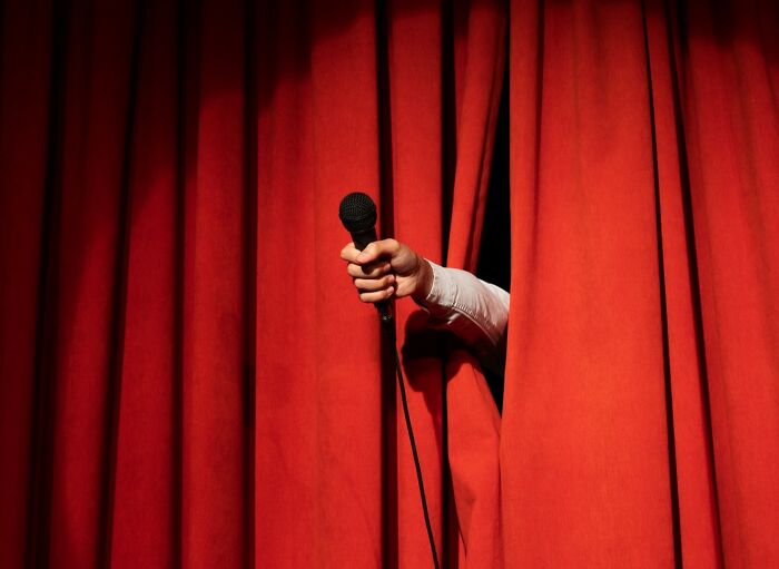 Hand holding a microphone emerging from behind a red curtain, symbolizing a good trend slowly disappeared.