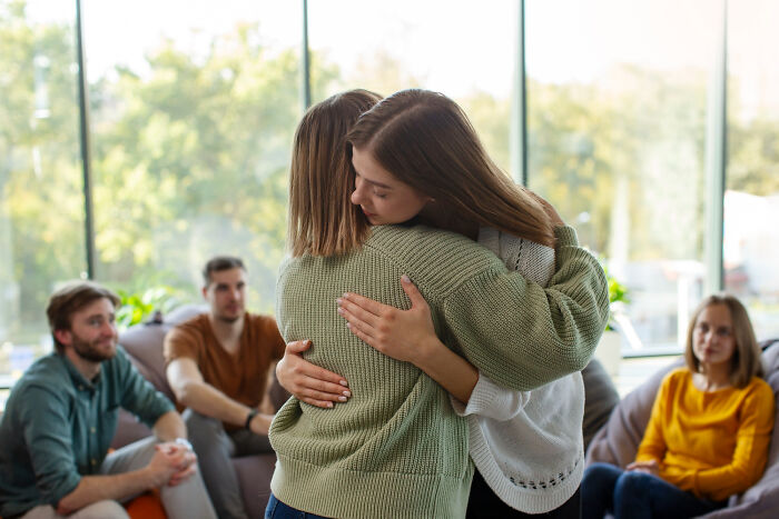 Two women hugging in a group setting, showing support as a good trend slowly disappeared among friends.