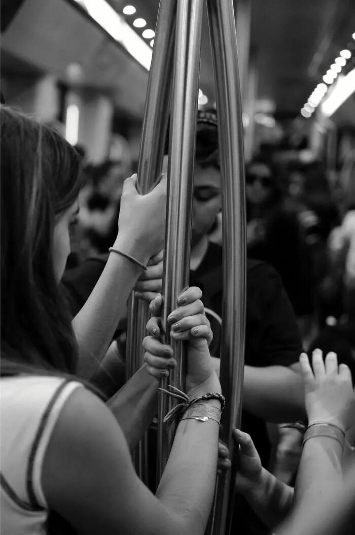 Black and white street shot showing hands holding metal poles inside a crowded public transit, capturing the poetry of everyday life.