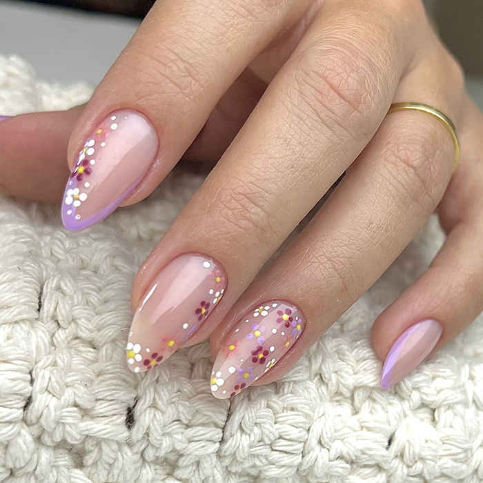 Close-up of summer nails with pink floral designs on a n**e base, showcasing a trendy and fresh look for 2025.