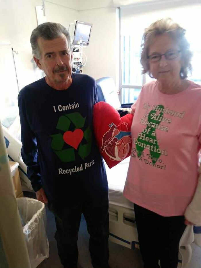 A man and woman in hospital room holding a red heart pillow, symbolizing heart donation and recycled parts.