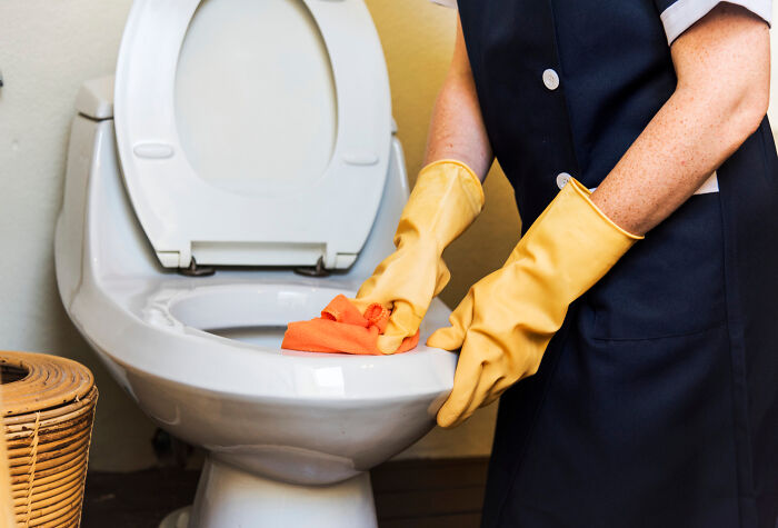 Person wearing yellow gloves cleaning a toilet, illustrating professions people think attract the most awful people.