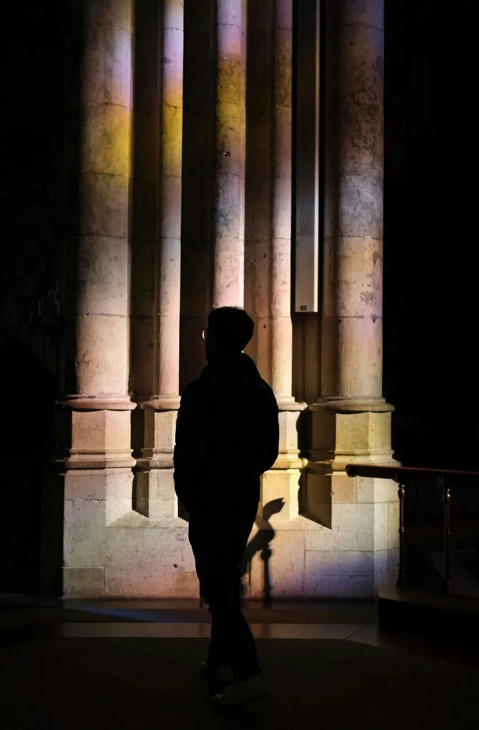 Silhouette of a person standing near illuminated stone columns, showcasing beautiful street shots capturing everyday life poetry.