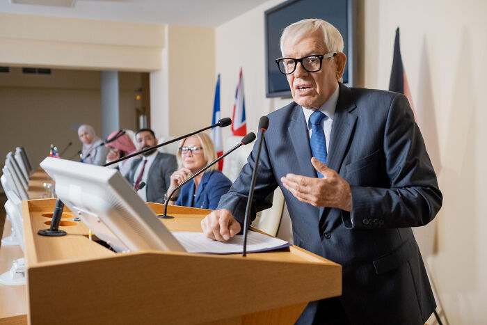 Elderly man in a suit speaking at a podium during a conference about a good trend slowly disappeared.