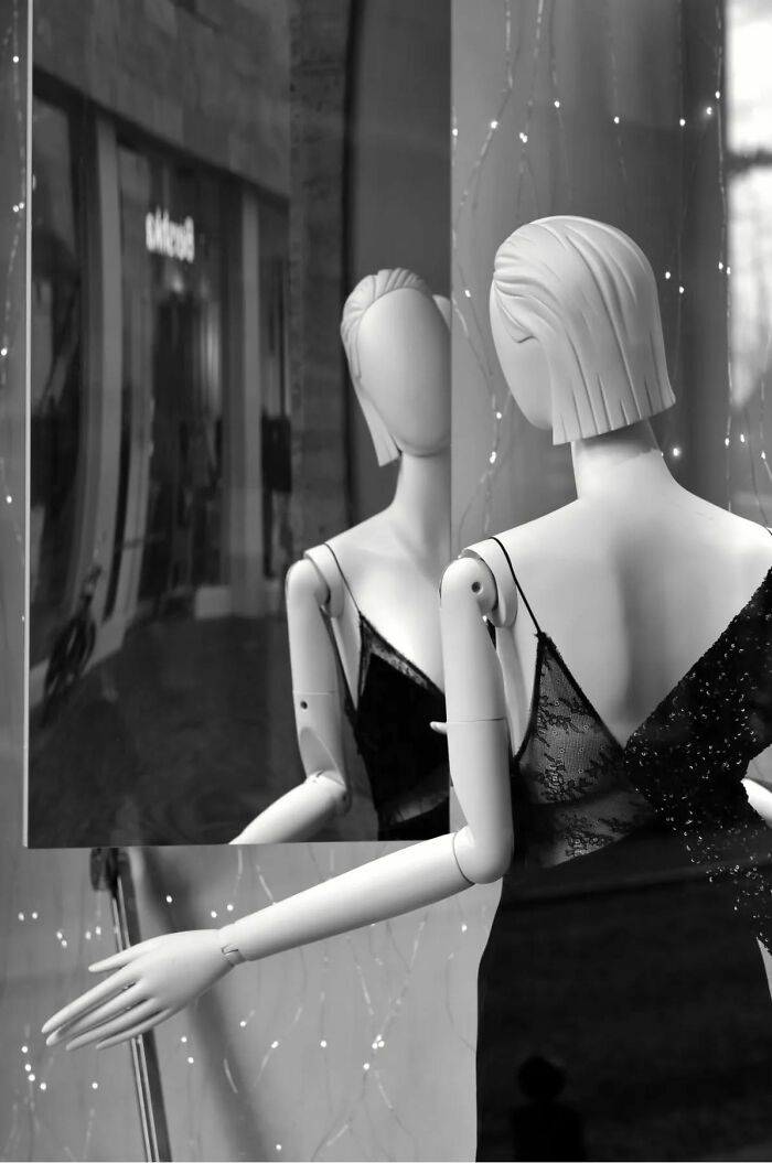 Mannequin wearing a black lace dress reflected in a mirror, showcasing beautiful street shots capturing everyday life poetry.