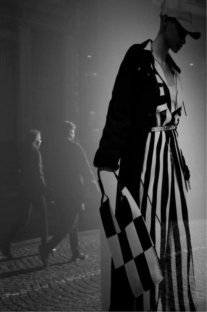 Black and white street shot of a fashionable person with striped clothing and bag, capturing the poetry of everyday life.