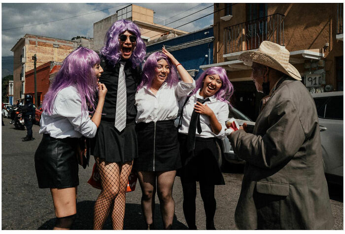 Group of friends in purple wigs and school uniforms laughing with an elderly man on urban Asian streets, capturing raw street moments.