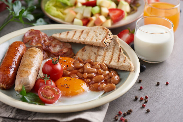 Traditional UK breakfast plate with sausages, eggs, baked beans, toast, and tomatoes, representing authentic UK cuisine.