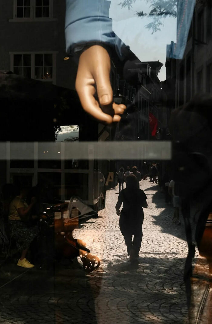 Street shot capturing the poetry of everyday life with silhouette of person walking on cobblestone street and reflections.