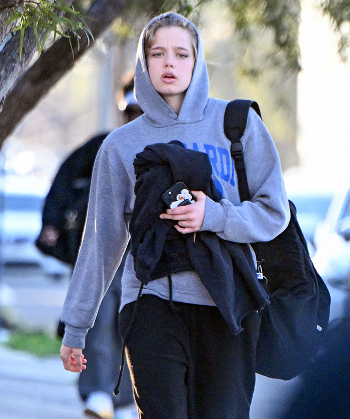 Young person in a grey hoodie walking outdoors, holding clothes and a phone, linked to Brad Pitt cutting off contact with sons news. Young person in a grey hoodie walking outdoors, holding clothes and a phone, linked to Brad Pitt cutting off contact with sons news.