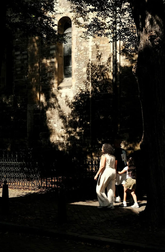 Street shots of a family walking near a sunlit stone building capturing the poetry of everyday life in shadows and light.