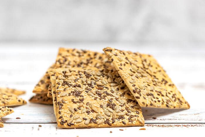 Crispy seed crackers stacked on a white wooden surface, illustrating best processed foods for weight loss. Crispy seed crackers stacked on a white wooden surface, illustrating best processed foods for weight loss.
